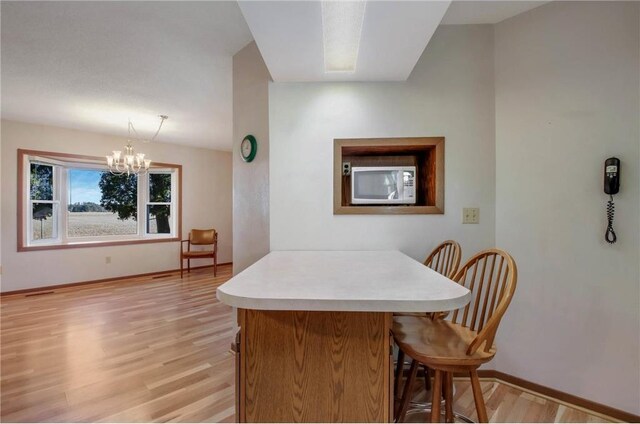 kitchen with a kitchen breakfast bar, light hardwood / wood-style floors, hanging light fixtures, and an inviting chandelier