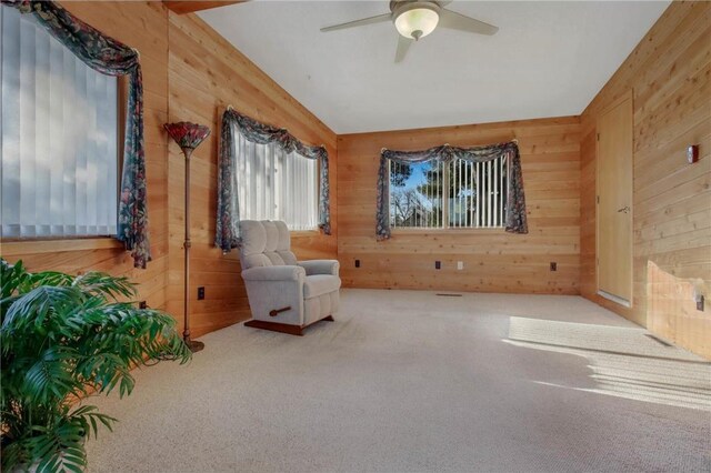 living area featuring ceiling fan, carpet floors, wooden walls, and lofted ceiling