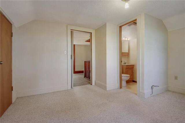 interior space with light carpet, a textured ceiling, vaulted ceiling, and connected bathroom