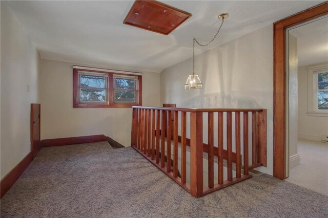 hall featuring plenty of natural light, light colored carpet, lofted ceiling, and an inviting chandelier