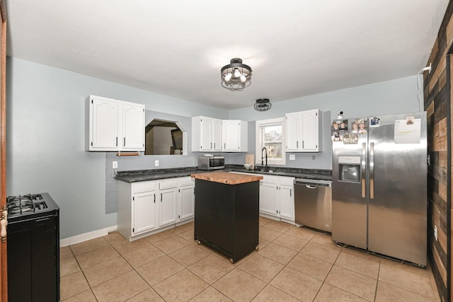 kitchen with appliances with stainless steel finishes, sink, light tile patterned floors, white cabinets, and a kitchen island