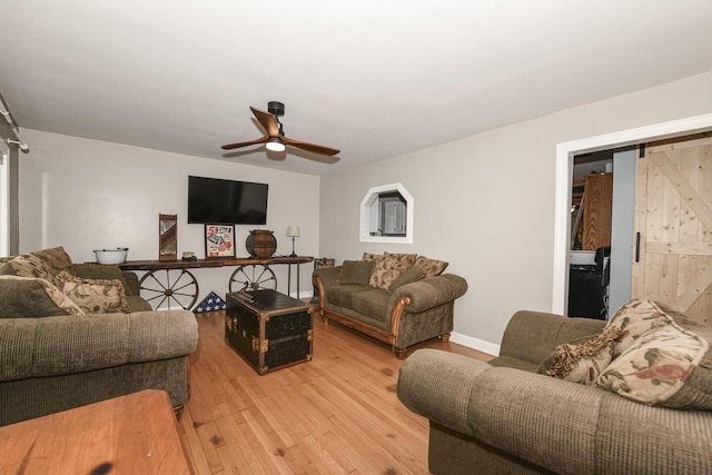 living room featuring ceiling fan, a barn door, and light wood-type flooring