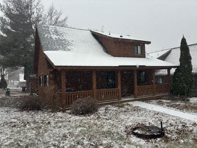 snow covered back of property featuring covered porch