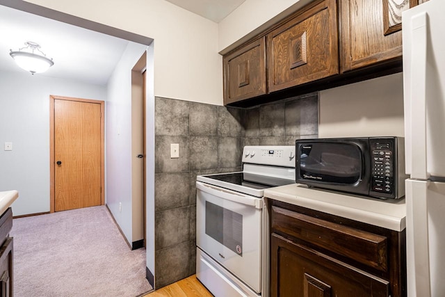 kitchen with dark brown cabinets, light colored carpet, and white appliances