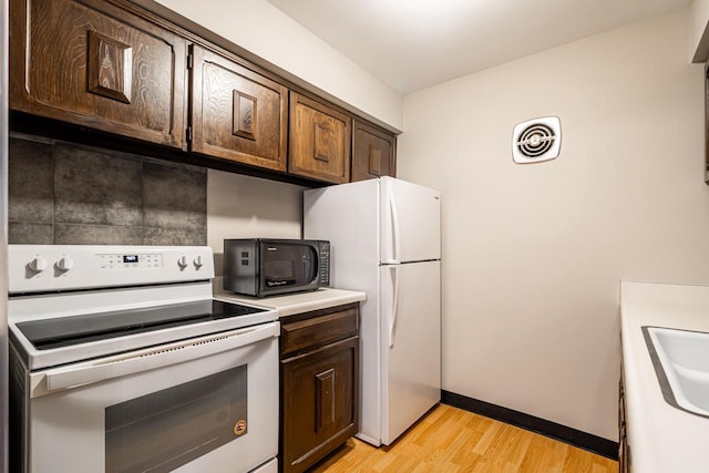 kitchen with dark brown cabinets, light hardwood / wood-style flooring, white appliances, and sink