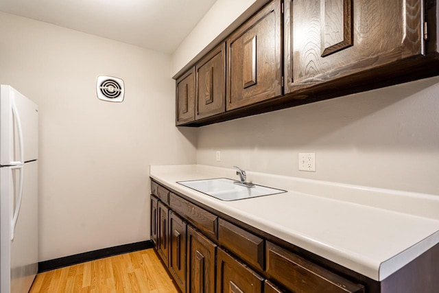 kitchen with dark brown cabinets, white fridge, light hardwood / wood-style flooring, and sink