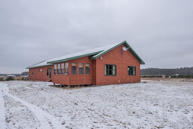 snow covered rear of property featuring a sunroom