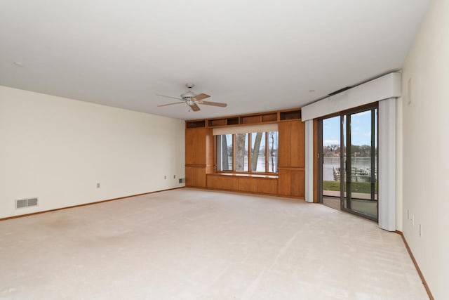 unfurnished room featuring ceiling fan, a water view, and light colored carpet