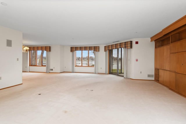 empty room with a notable chandelier, a healthy amount of sunlight, and light colored carpet