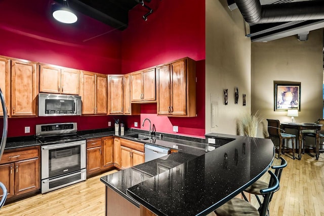 kitchen with dark stone counters, sink, a towering ceiling, appliances with stainless steel finishes, and light hardwood / wood-style floors