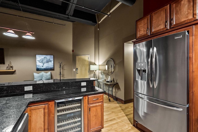 kitchen with stainless steel refrigerator with ice dispenser, a towering ceiling, beverage cooler, dark stone countertops, and light hardwood / wood-style floors