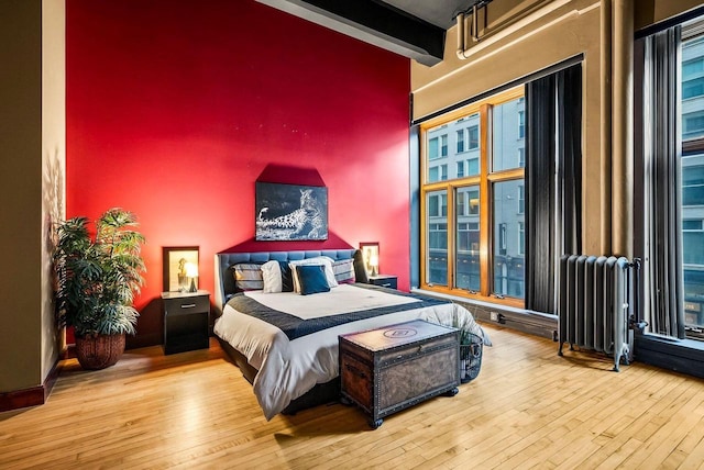 bedroom featuring beam ceiling, radiator heating unit, a towering ceiling, and wood-type flooring