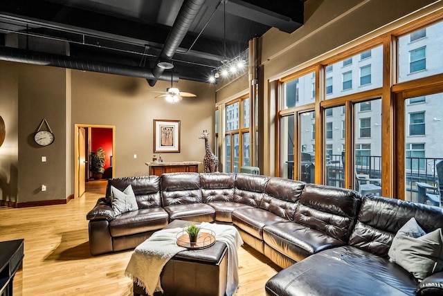 living room featuring ceiling fan, light wood-type flooring, and a high ceiling