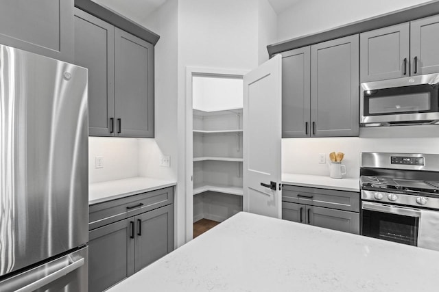 kitchen with light stone countertops, appliances with stainless steel finishes, and gray cabinets