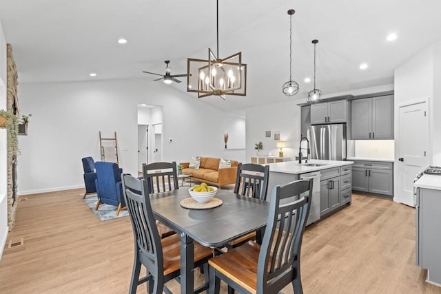 dining space with ceiling fan with notable chandelier, sink, light hardwood / wood-style flooring, and vaulted ceiling