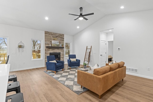 living room with light hardwood / wood-style floors, a stone fireplace, ceiling fan, and lofted ceiling