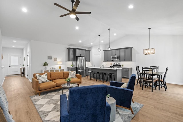 living room with ceiling fan with notable chandelier, light hardwood / wood-style flooring, vaulted ceiling, and sink