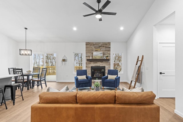 living room featuring ceiling fan with notable chandelier, light hardwood / wood-style floors, and a stone fireplace