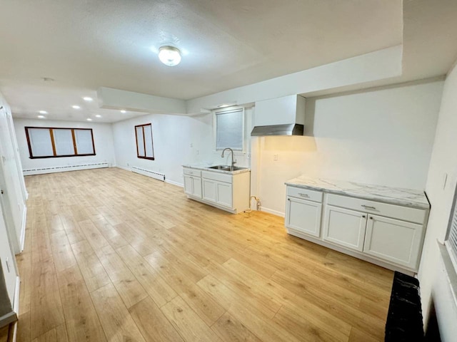 interior space featuring white cabinets, wall chimney range hood, sink, and a baseboard heating unit