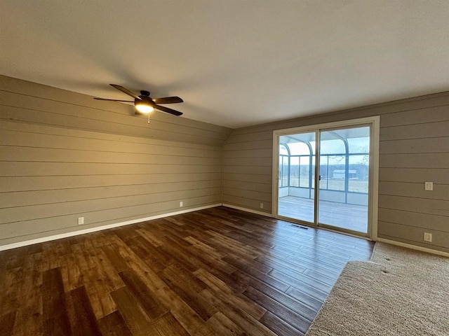 spare room with dark hardwood / wood-style floors, ceiling fan, and wood walls