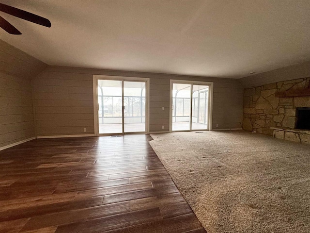 unfurnished living room featuring dark hardwood / wood-style flooring, ceiling fan, wooden walls, a fireplace, and lofted ceiling