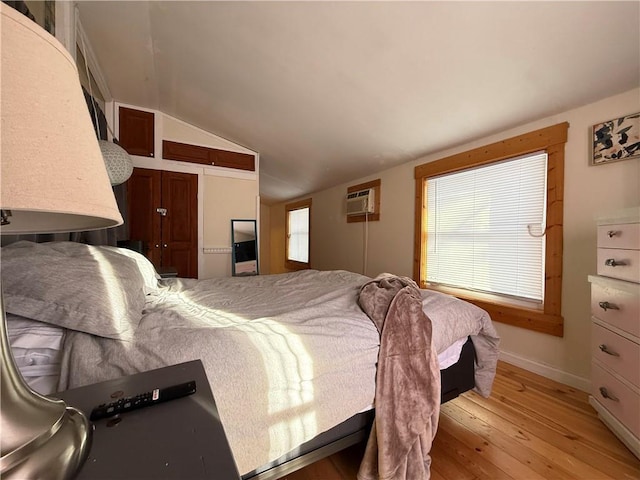 bedroom with light hardwood / wood-style floors, vaulted ceiling, and an AC wall unit