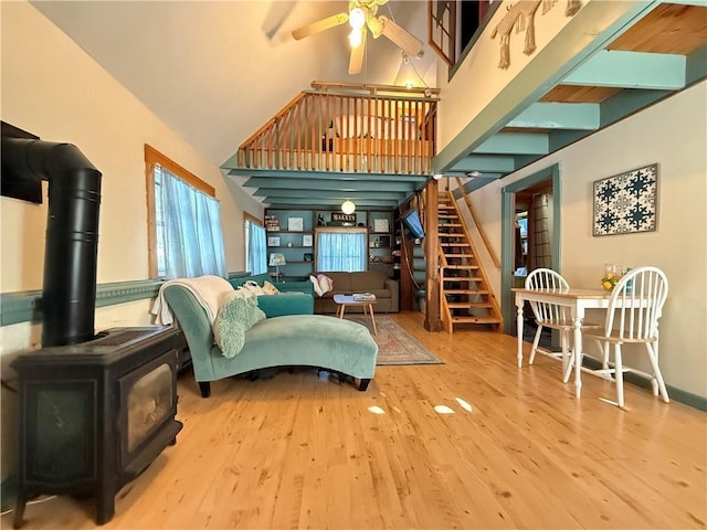 living room with hardwood / wood-style flooring, ceiling fan, a wood stove, and high vaulted ceiling