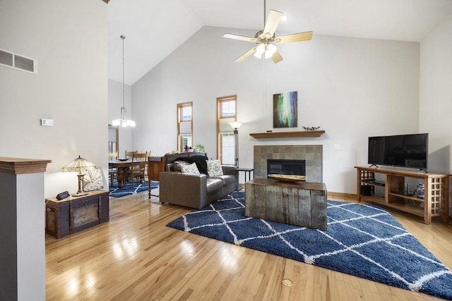 living room with ceiling fan with notable chandelier, hardwood / wood-style flooring, high vaulted ceiling, and a tiled fireplace