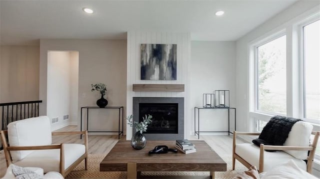 living room with light wood-type flooring, a large fireplace, and plenty of natural light