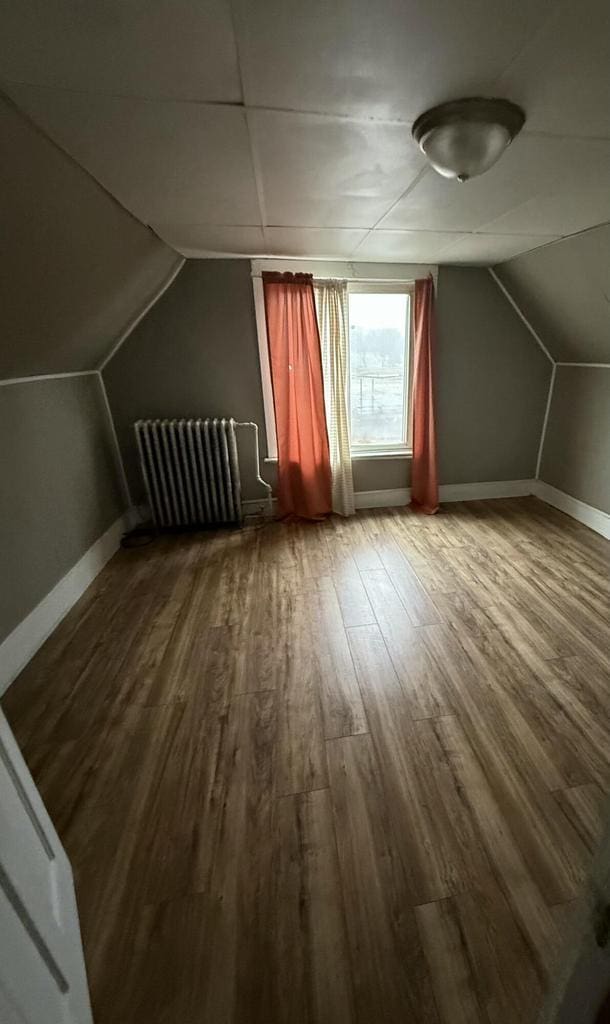 bonus room featuring baseboards, vaulted ceiling, radiator heating unit, and wood finished floors