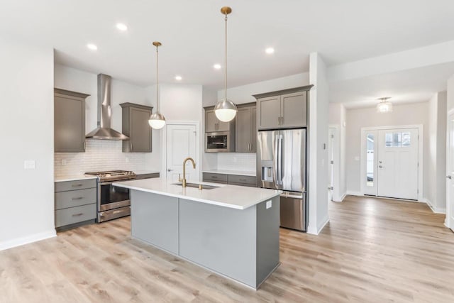 kitchen featuring hanging light fixtures, sink, wall chimney exhaust hood, appliances with stainless steel finishes, and light hardwood / wood-style floors