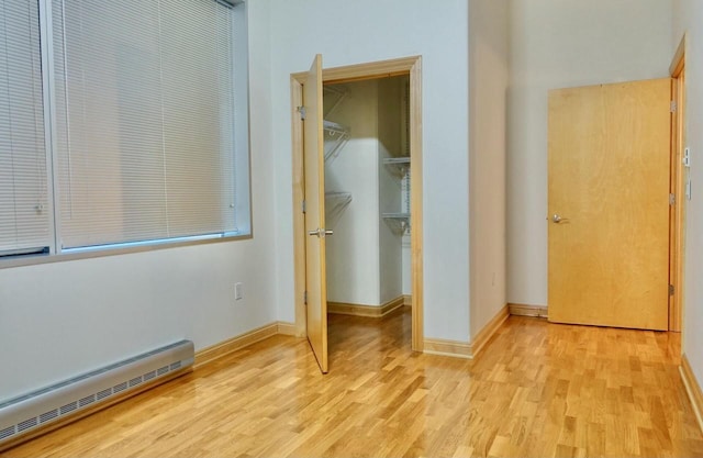 unfurnished bedroom featuring baseboard heating, a walk in closet, a closet, and light hardwood / wood-style flooring