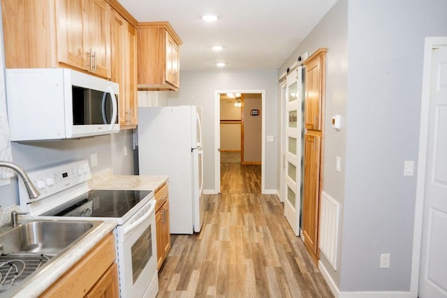 kitchen with light brown cabinets, white appliances, sink, a barn door, and light wood-type flooring