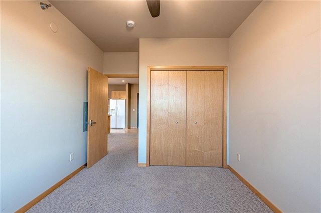 unfurnished bedroom featuring ceiling fan, white refrigerator with ice dispenser, light carpet, and a closet