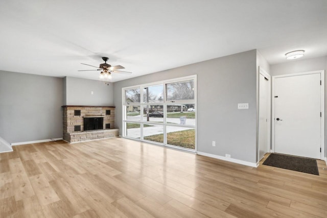 unfurnished living room with a stone fireplace, ceiling fan, and light hardwood / wood-style floors