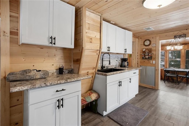 kitchen featuring wood walls, dark wood-type flooring, sink, light stone countertops, and white cabinetry