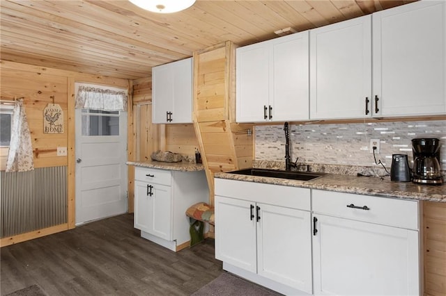 kitchen with white cabinets, wooden walls, and sink