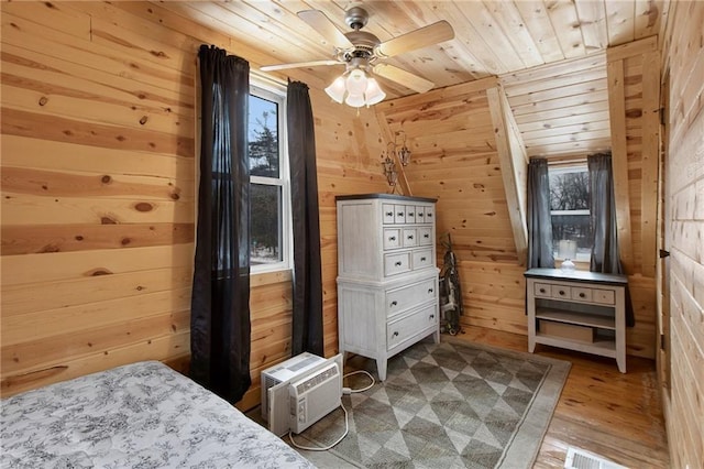 bedroom with hardwood / wood-style floors, ceiling fan, wooden walls, and multiple windows