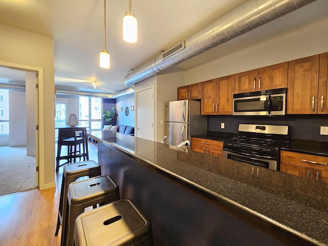 kitchen featuring a breakfast bar, dark stone counters, hanging light fixtures, light hardwood / wood-style floors, and stainless steel appliances