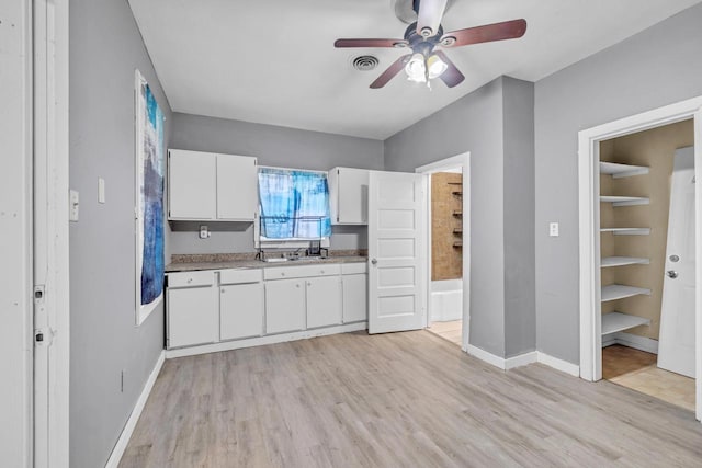 kitchen with light wood-type flooring, white cabinetry, ceiling fan, and sink