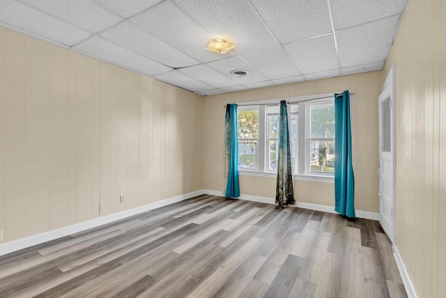 unfurnished room featuring a paneled ceiling, light hardwood / wood-style floors, and wood walls