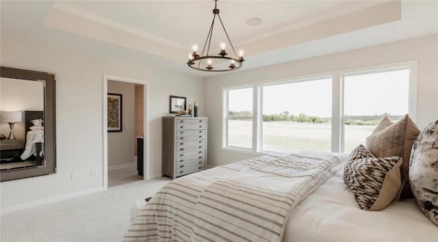 carpeted bedroom featuring a tray ceiling, an inviting chandelier, and a water view