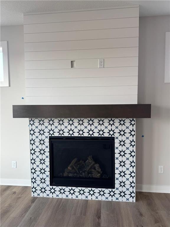 details featuring a textured ceiling, wood finished floors, a tile fireplace, and baseboards