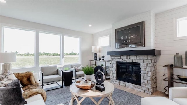 living room with light wood-type flooring, a stone fireplace, and wooden walls