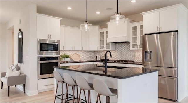 kitchen featuring sink, an island with sink, appliances with stainless steel finishes, decorative light fixtures, and white cabinetry