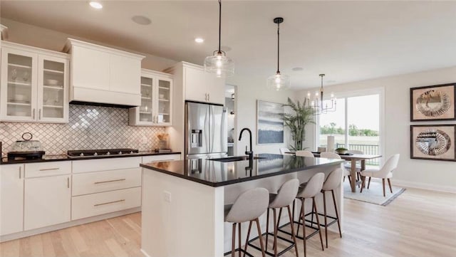 kitchen with a kitchen island with sink, sink, decorative light fixtures, white cabinetry, and stainless steel appliances