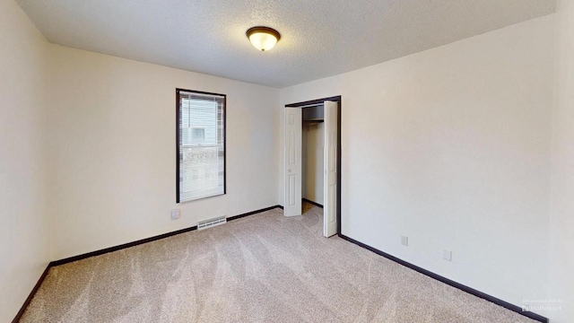 unfurnished room with a textured ceiling and light colored carpet