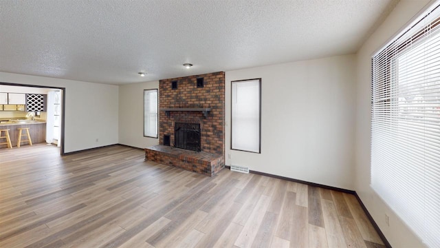 unfurnished living room featuring hardwood / wood-style floors, a textured ceiling, and a brick fireplace