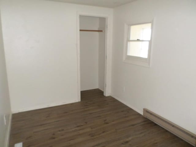 unfurnished bedroom with a closet, dark hardwood / wood-style floors, and a baseboard heating unit