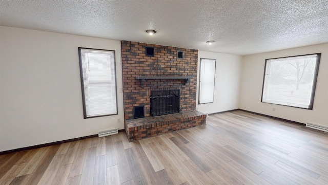 unfurnished living room featuring light hardwood / wood-style flooring, a textured ceiling, and a brick fireplace